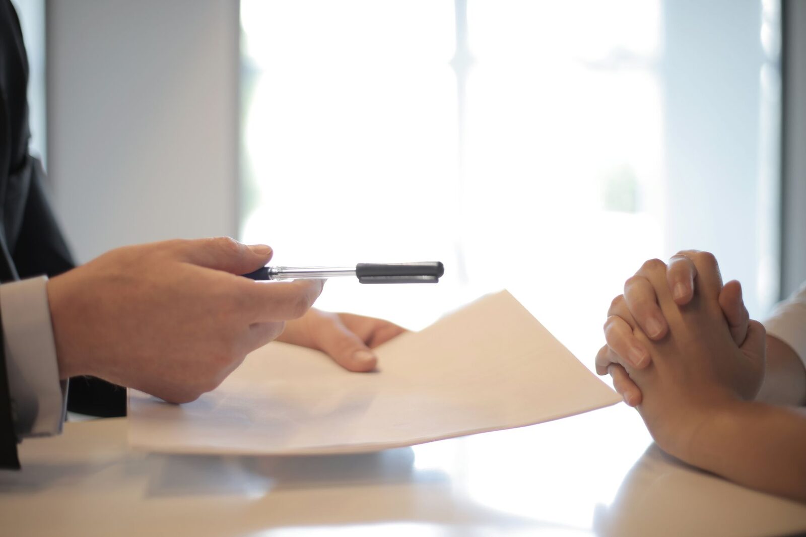 Side view of faceless formal man giving pen and paper to focused female with clenched hands at table on meeting